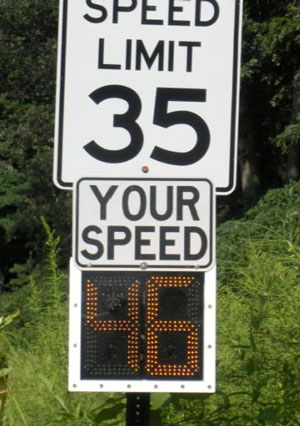 Photo. A typical speed limit sign posting 35 is shown with a digital display underneath. The display says, “your speed” and then has a dynamic number – 46 in this case.